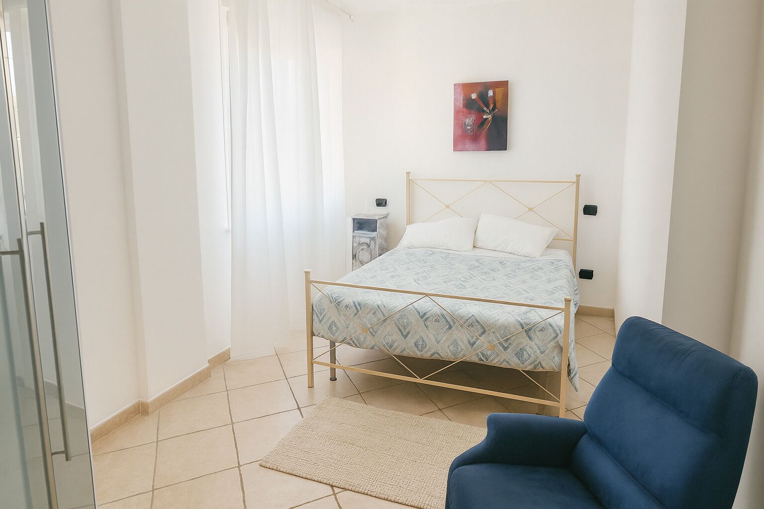 A bedroom with a bed, a chair, a nightstand, and a painting on the wall.