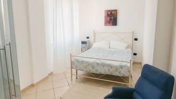 Ein Schlafzimmer mit einem Bett, einem Sessel, einem Nachttisch und einem Bild an der Wand.