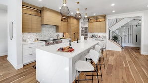 Una cocina moderna con armarios blancos, una isla grande con taburetes altos y lámparas colgantes.