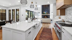 Una cocina moderna con armarios blancos, una isla grande, horno empotrado e iluminación colgante.