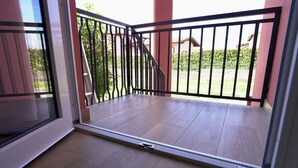 A balcony with a metal railing, a sliding glass door, and a view of a garden and a building in the background. - Maison 54 - Canneto Lake (Brescia)
