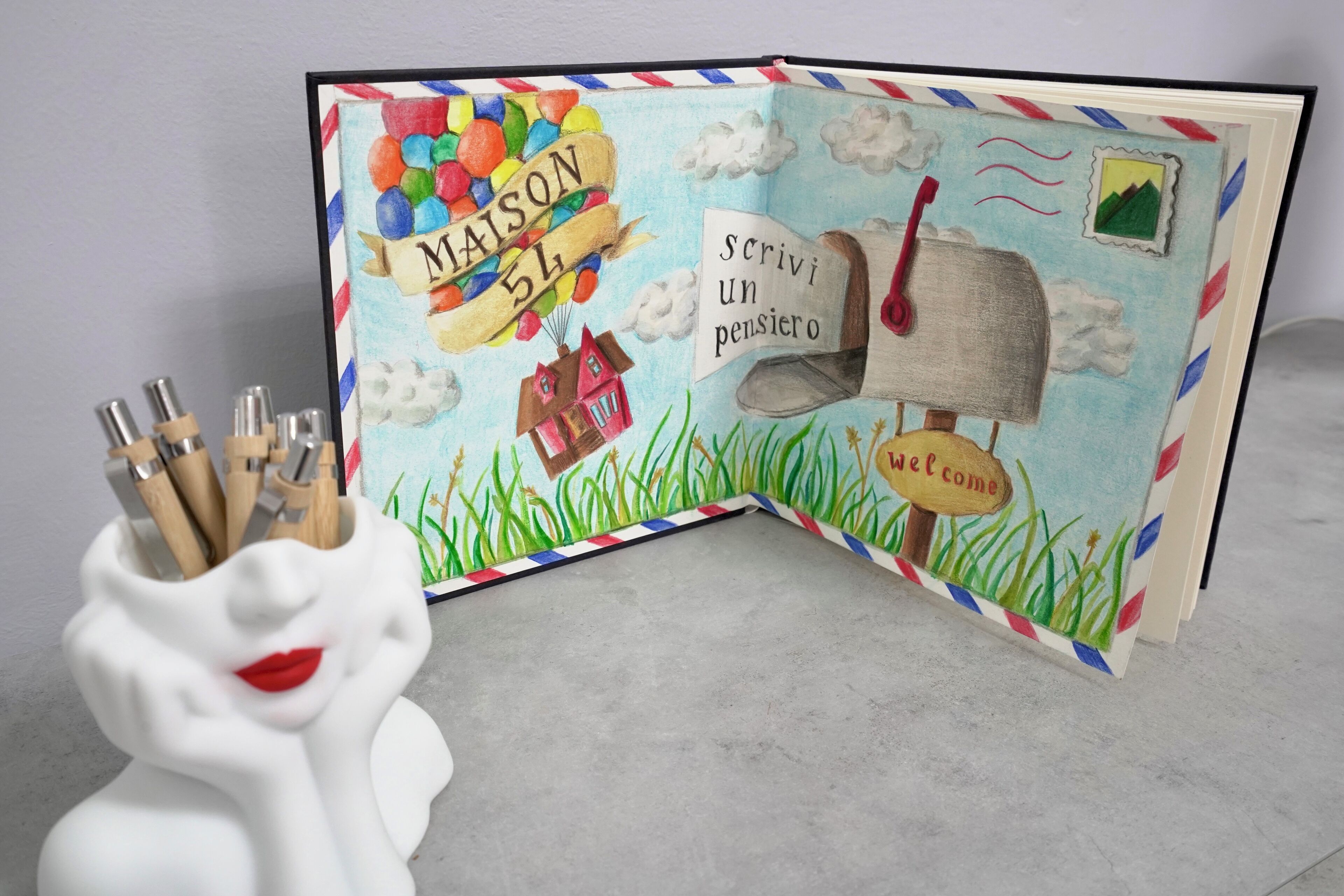 An open book with a colorful illustration of a house, balloons, and clouds.