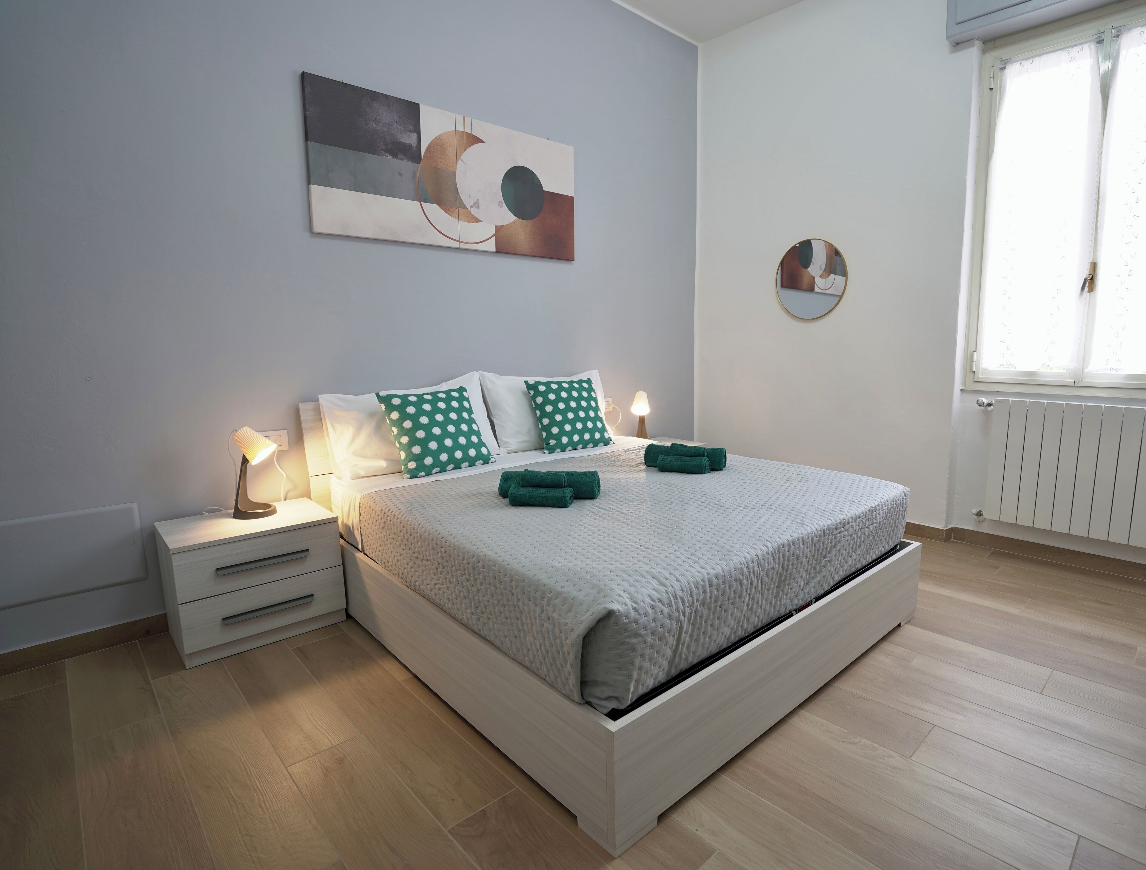 Una camera da letto moderna con un letto, comodini, un’opera d’arte appesa al muro e una finestra con tende.