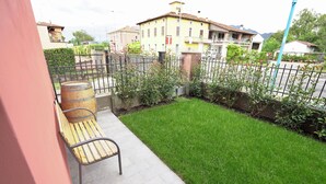 A patio with a wooden bench, a barrel, and a small lawn. - Maison 54 - Canneto Lake (Brescia)