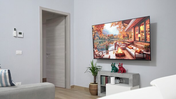 A modern living room with a large flat-screen TV mounted on the wall, a grey sofa, a small side table with decorative items, and a wooden door. - Maison 54 - Canneto Lake (Brescia)