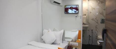 Habitación de hotel con cama, una silla, televisión y baño con ducha e inodoro.