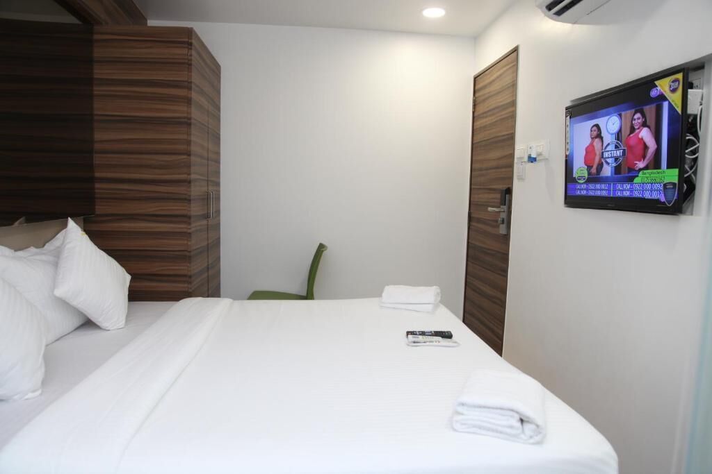 A hotel room with a bed, a TV mounted on the wall, and a wooden wardrobe.