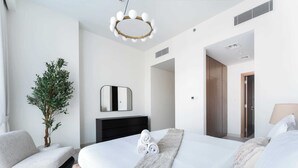 A modern bedroom with a large bed, a bedside table, a mirror, a potted plant, and a hanging light fixture.
