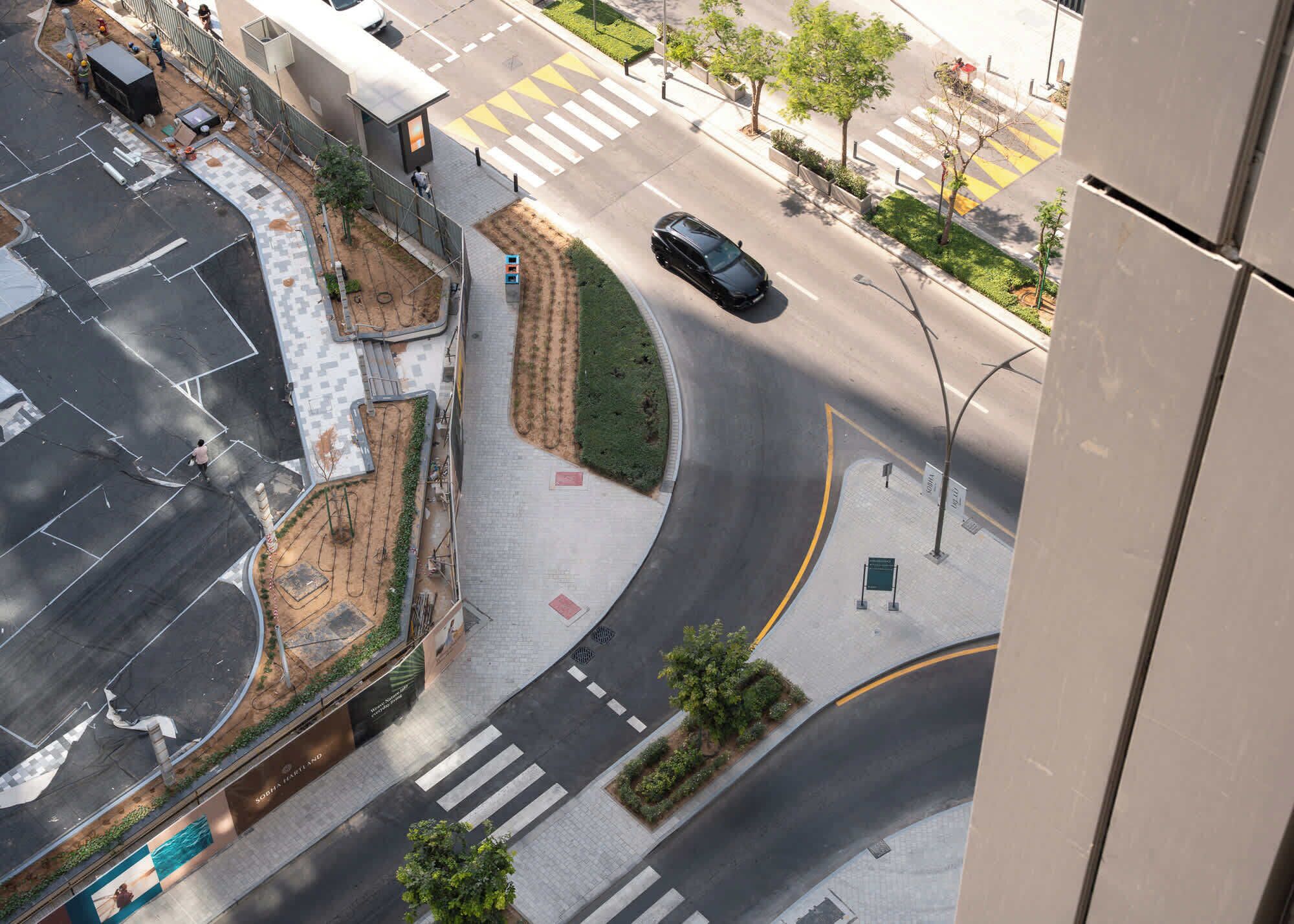 An aerial view of a city intersection with a curved road, pedestrian crossings, and greenery.