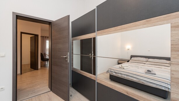 A modern bedroom with a bed, a mirror, and a door leading to another room. - Beachside Holiday Home Anamarija (Lozice)