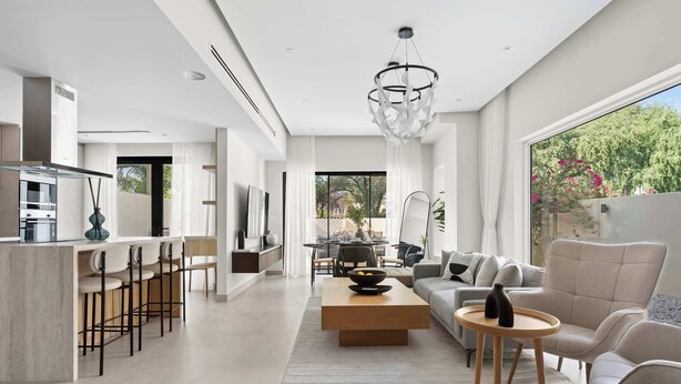 Un salon moderne avec un canapé, une table basse et des tabourets de bar. On y trouve également un coin repas avec une table et des chaises, ainsi qu'une cuisine équipée d'une cuisinière et de placards.