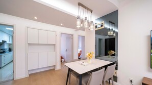Une cuisine moderne avec des meubles blancs, une table à manger avec des chaises et des luminaires suspendus.