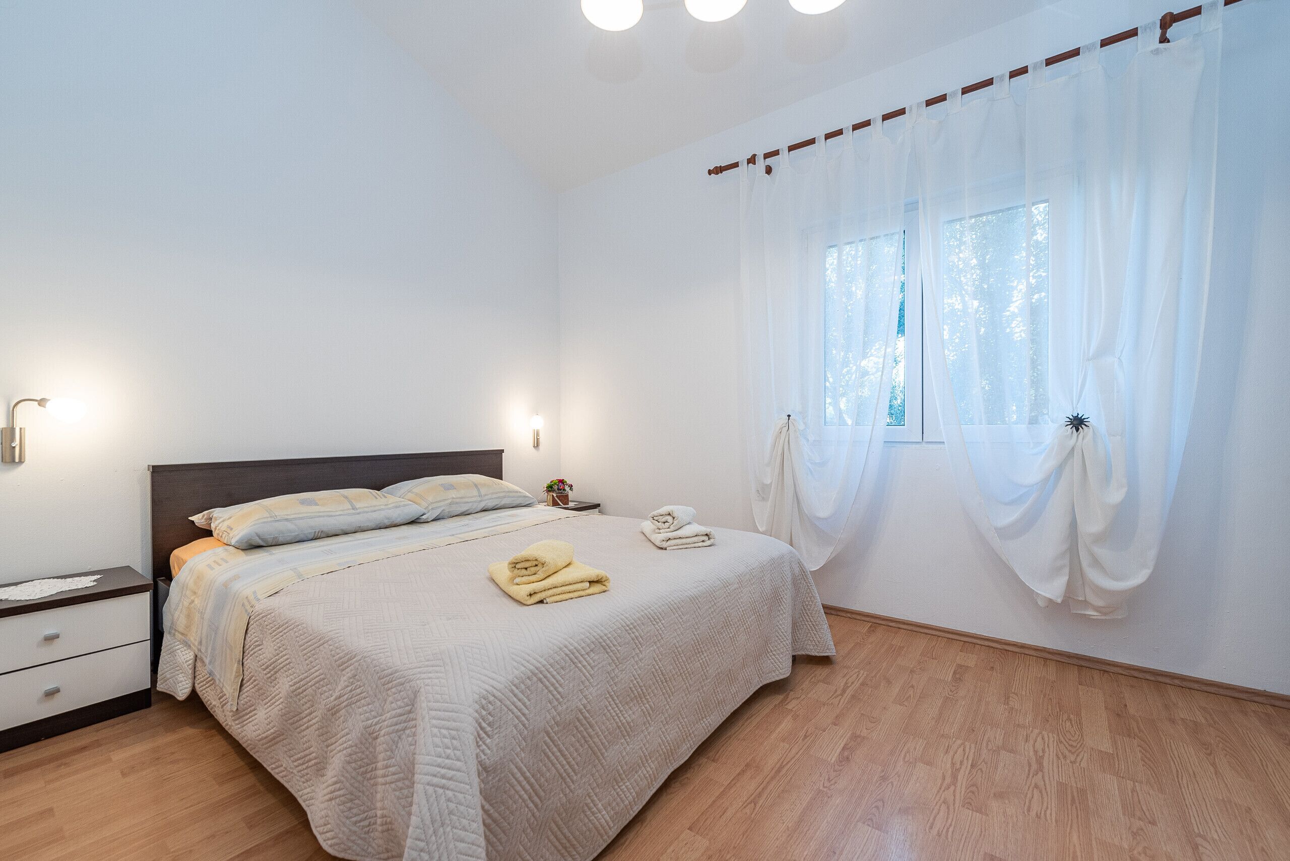Quarto com cama, mesa de cabeceira e janela com cortinas.