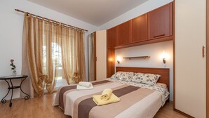 A bedroom with a double bed, wooden headboard, bedside lamps, a small table with a vase, and sheer curtains. - Beachside Holiday Home Manuela (Lozice)