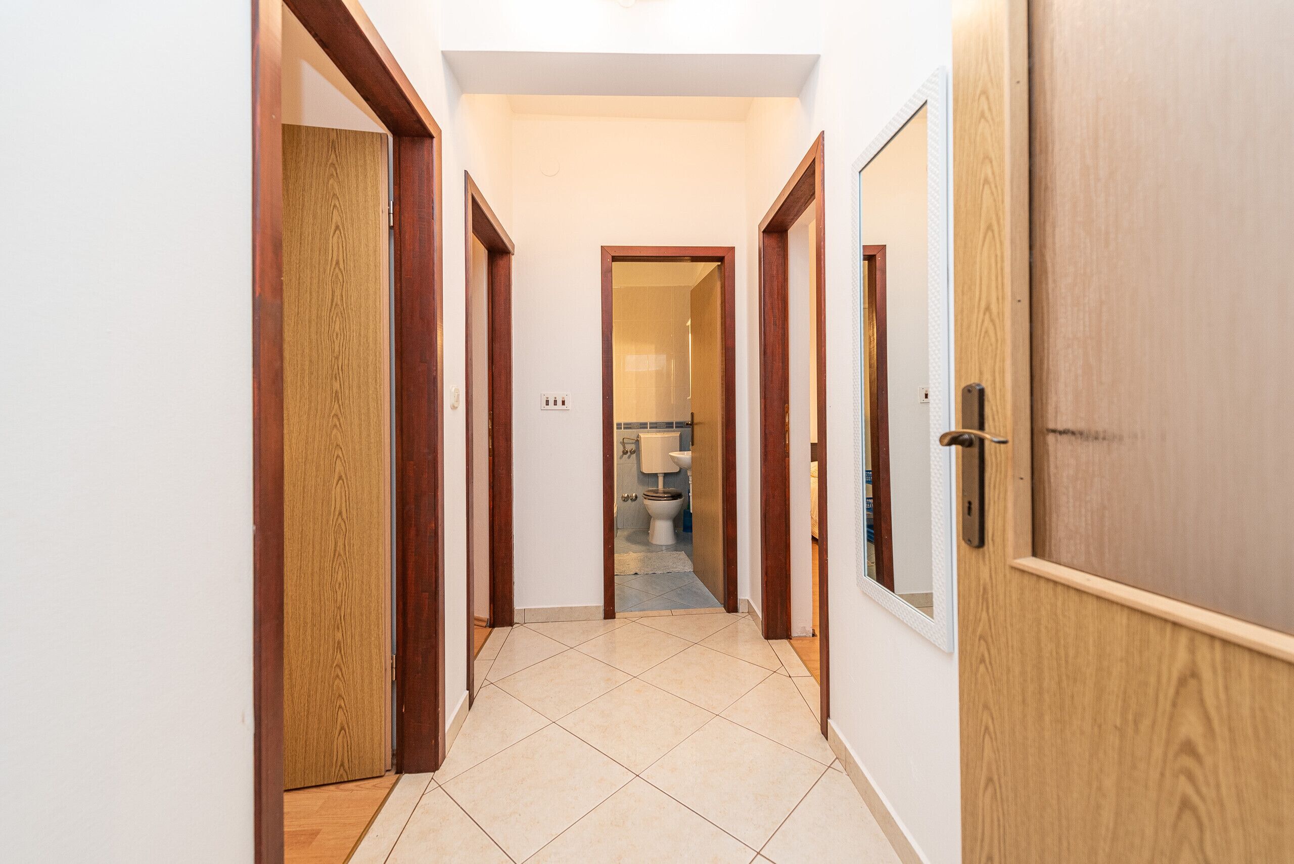 Un couloir avec des portes en bois et un sol carrelé qui mène à une salle de bain.