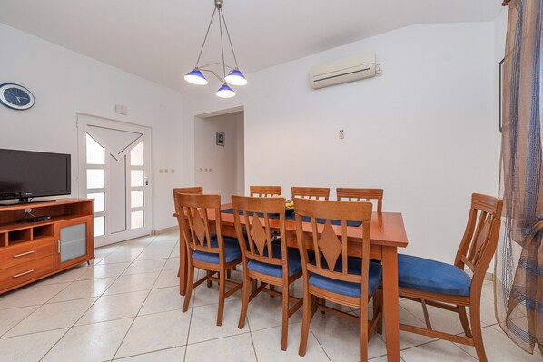 A dining area with a wooden table and chairs, a television on a cabinet, and an air conditioning unit on the wall.