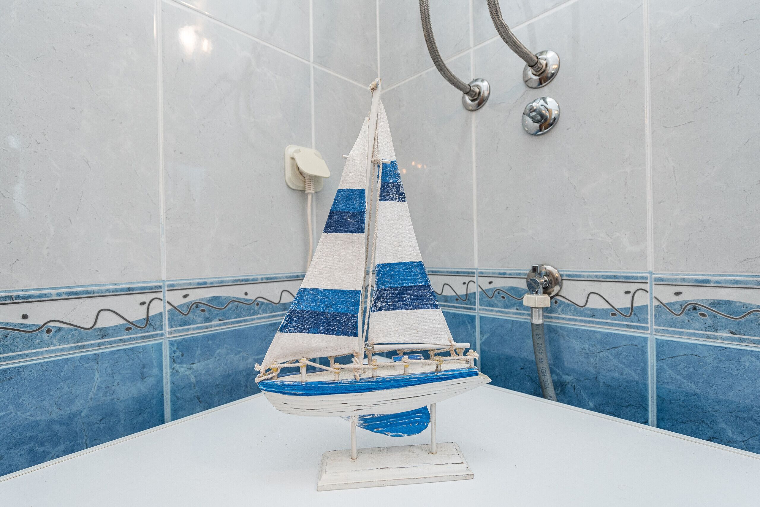 A model sailboat on a white table in a bathroom with blue and white tiled walls.