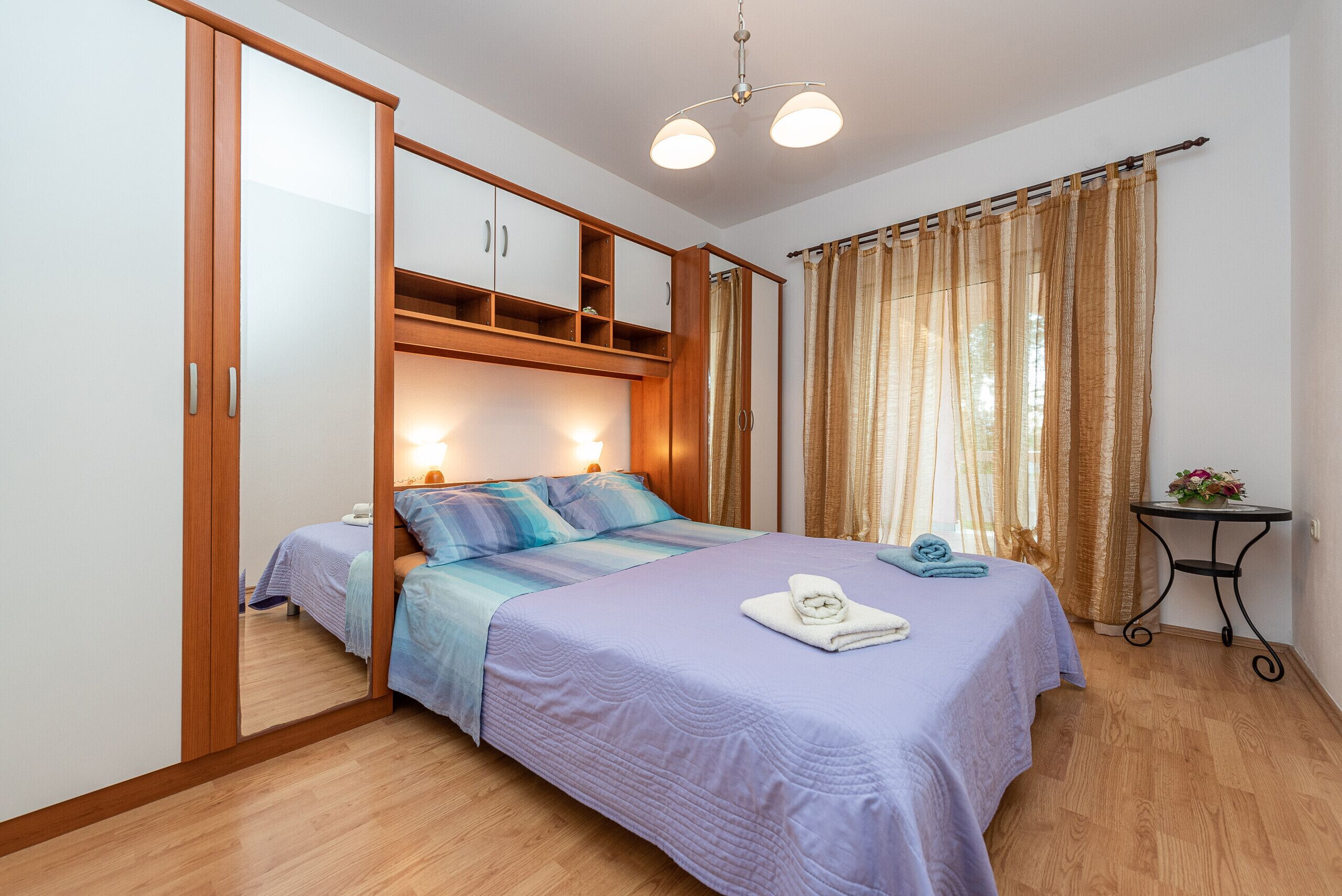 Ein Schlafzimmer mit Bett, Kleiderschrank, Nachttisch und einem Fenster mit Vorhängen.