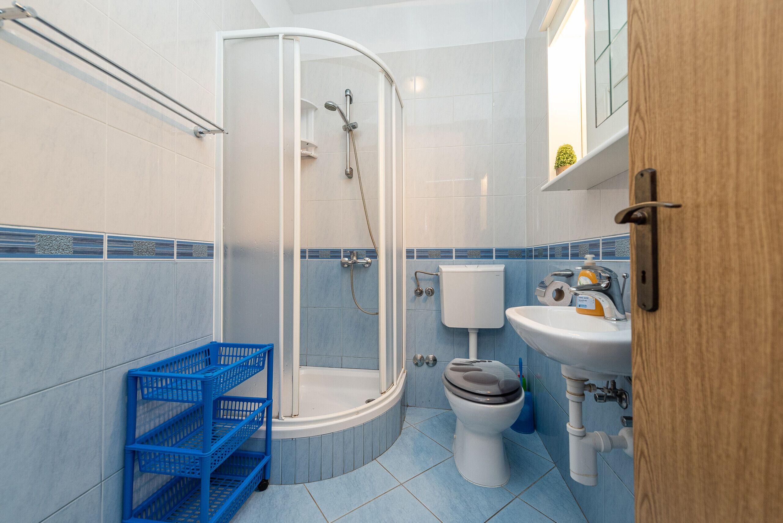 A bathroom with a shower, toilet, sink, and blue tiled walls.