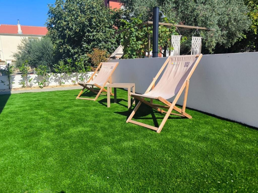 Deux fauteuils de jardin en bois, placés sur une pelouse bien entretenue, avec un mur gris et de la verdure en arrière-plan.