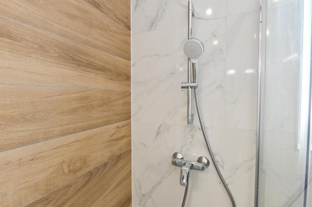 A bathroom with a wooden floor and a shower with a marble wall.