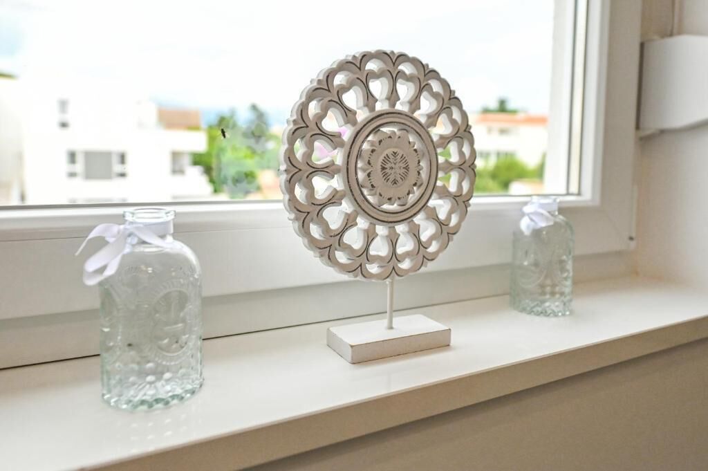 Un élément décoratif en métal posé sur un rebord de fenêtre, accompagné de deux bouteilles en verre transparent.