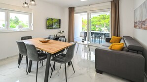 Ein modernes Wohnzimmer mit Essbereich, einem grauen Sofa mit gelben Kissen und einem großen Fenster mit Blick auf Grünflächen.