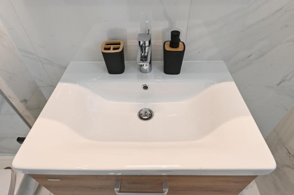 A bathroom with a white sink, a chrome faucet, and two black soap dispensers with wooden tops.