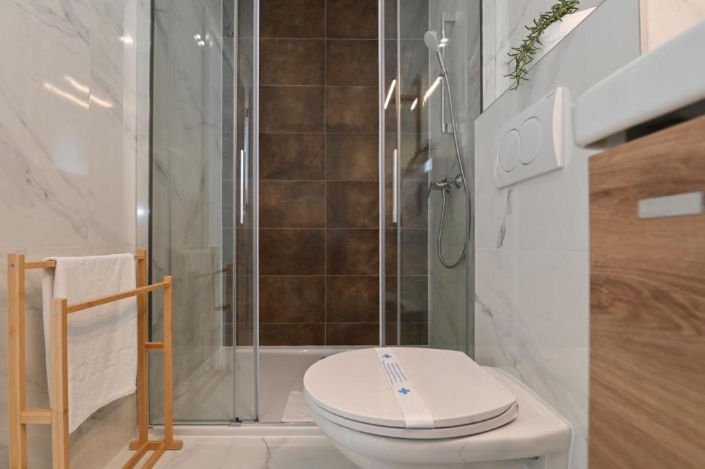Een moderne badkamer met een glazen douchecabine, een houten handdoekhouder en een toilet met bedieningspaneel.
