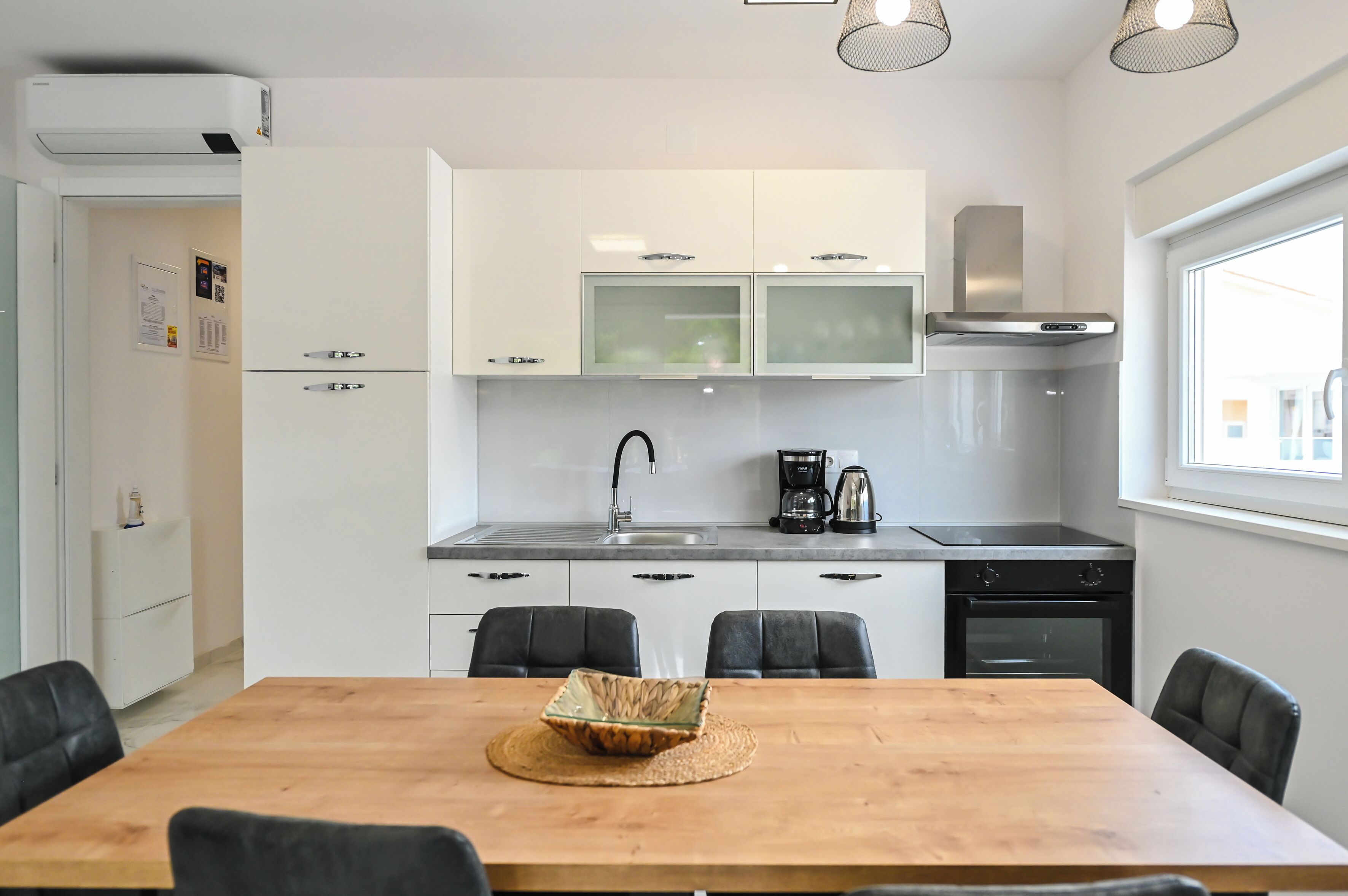 A modern kitchen with white cabinets, a stainless steel sink, and a black stove. There is a dining table with four chairs in front.