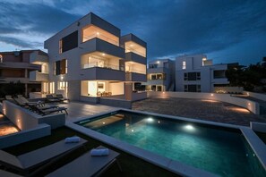 Un immeuble moderne à plusieurs étages, doté d’une piscine et d’un espace extérieur aménagé pour se détendre.