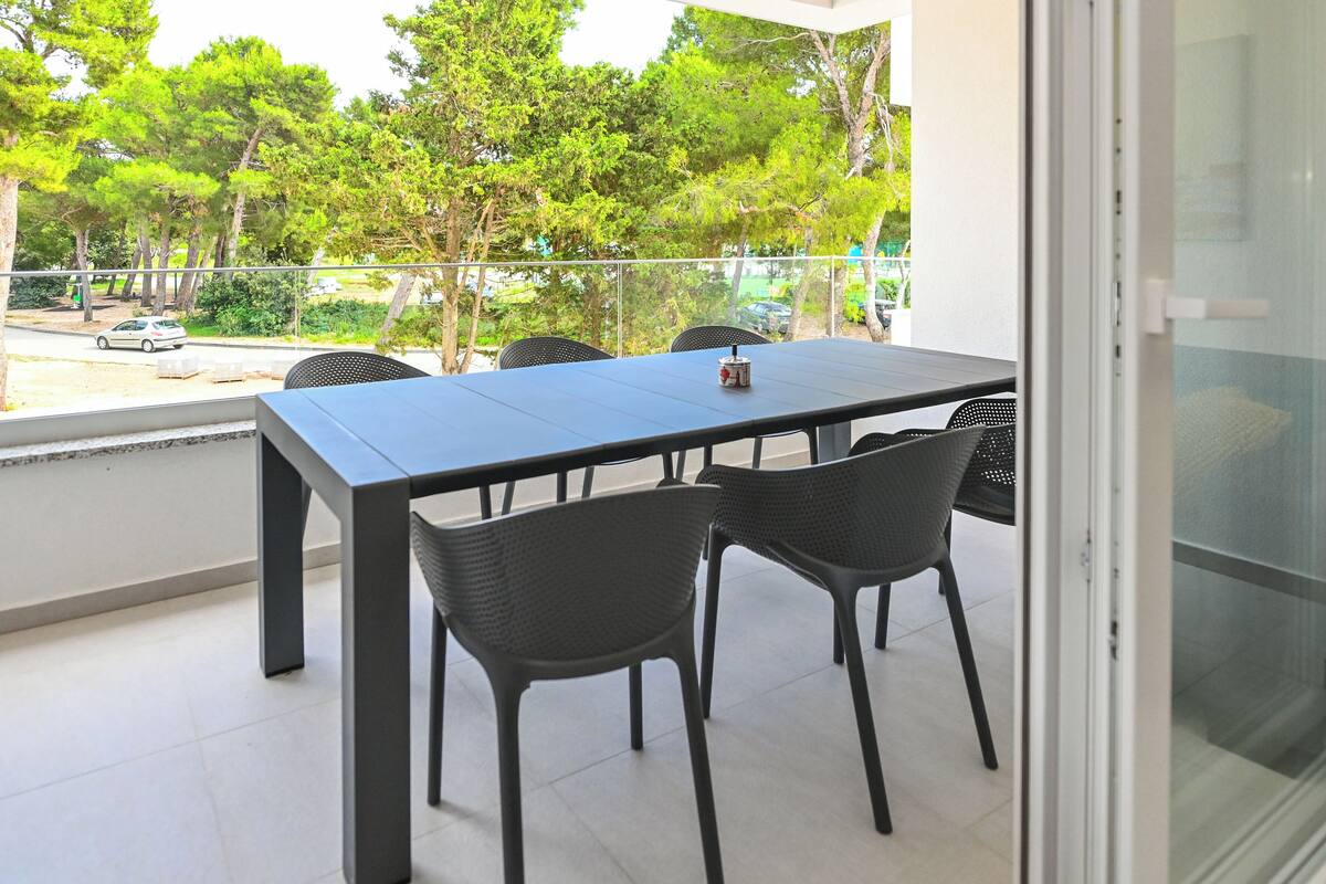 A balcony with a table and chairs, overlooking a street and trees.