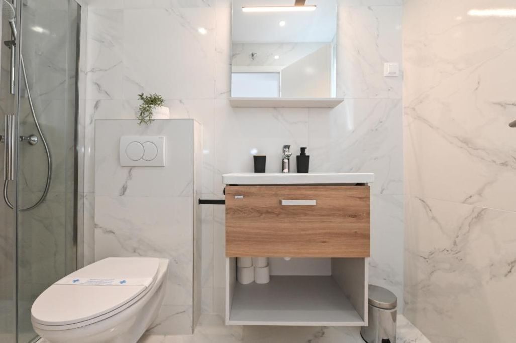 A modern bathroom with a white toilet, a wooden vanity with a mirror, and a shower area.