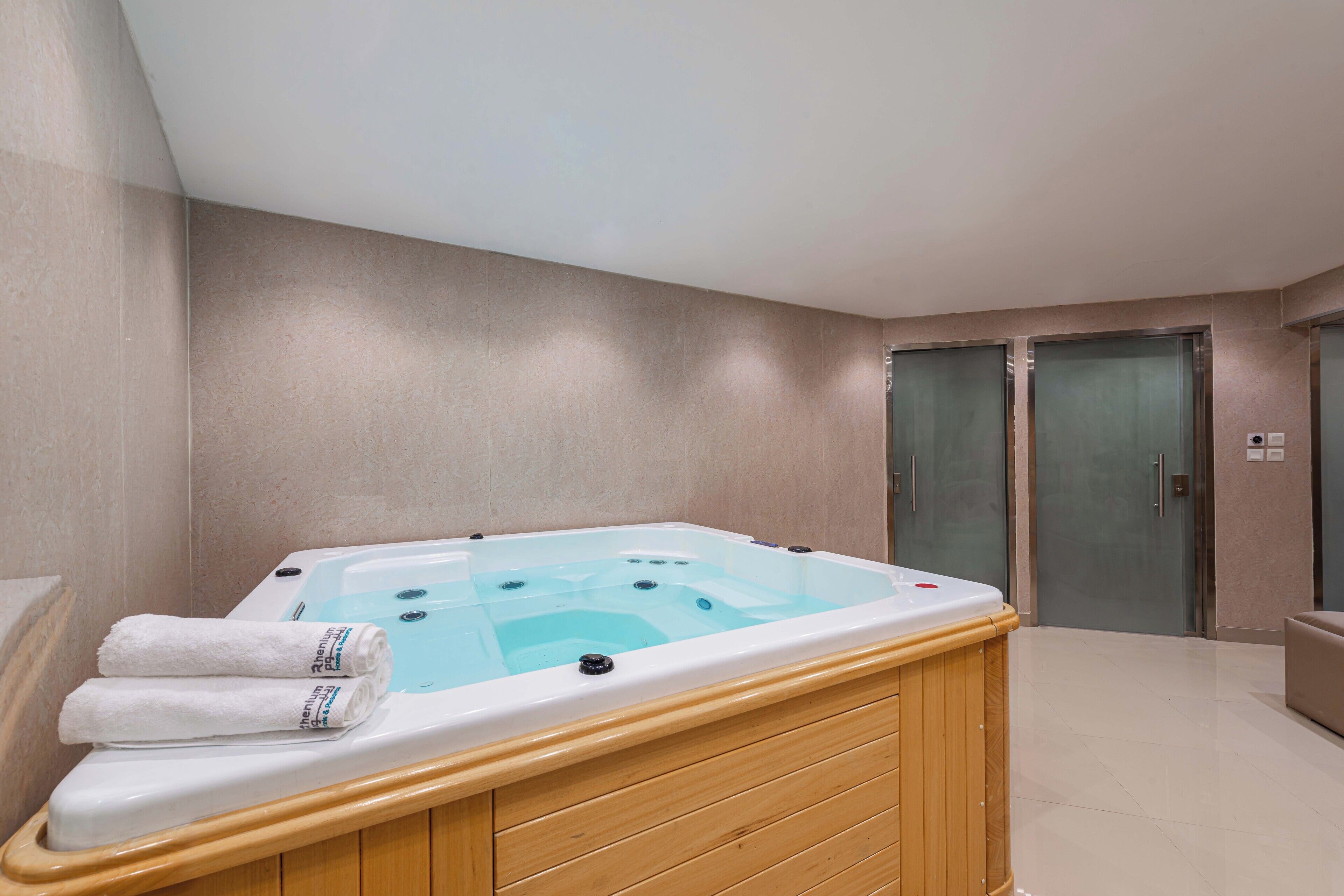 A modern bathroom with a wooden bathtub, two doors, and a tiled floor.
