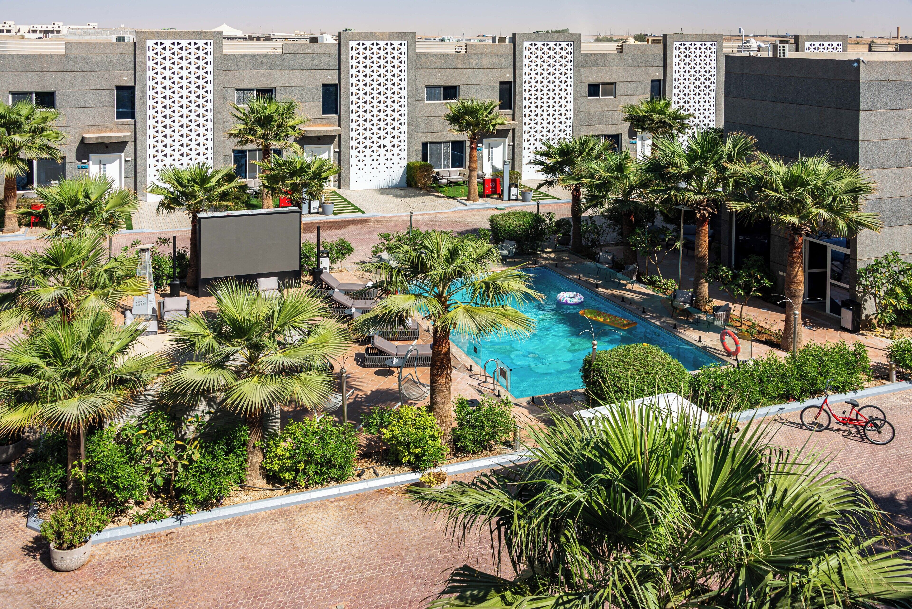 A rooftop pool area with palm trees, lounge chairs, and a bicycle.