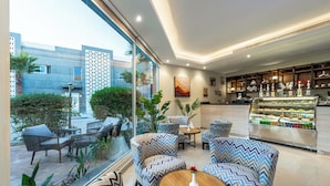 A modern hotel lobby with zigzag patterned chairs, a glass display case with food items, and a view of the outside.