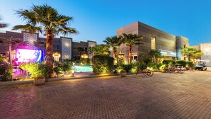 A paved courtyard with palm trees, a pool, and a modern building with a flat roof.