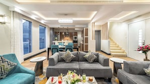 A modern living room with a grey sofa set, a coffee table with drinks, and a dining area in the background.