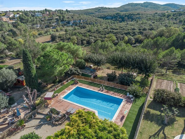 A swimming pool surrounded by a wooden fence, with a patio area and a view of a hilly landscape.