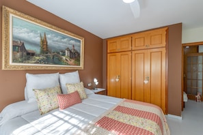 A bedroom with a bed, pillows, a nightstand, a painting, and a wardrobe.
