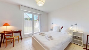 A bedroom with a bed, a desk, a chair, and a nightstand with lamps.