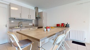 A modern kitchen with a wooden island, white chairs, and stainless steel appliances.
