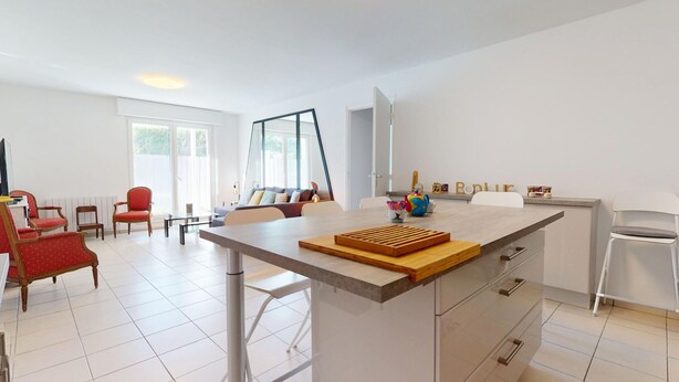 A modern kitchen with a central island, white cabinetry, and a dining area with red upholstered chairs.