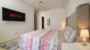A bedroom with a bed, a bedside lamp, a wall-mounted TV displaying the Netflix logo, and a door leading to another room. - Chic and contemporary, comfort guaranteed. (Agadir)