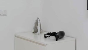 A white bedside table with a modern iron and a black electronic device, possibly a portable speaker, on top.