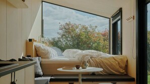 A compact, modern kitchen with a built-in bench and a small table, large windows offering a view of trees and sky. - Raus | Cabins mit Feldblick + Saunazugang (Königslutter am Elm)