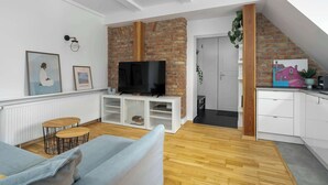 A modern living room with a brick fireplace, white cabinetry, and a flat-screen TV. - Stylish Apartment with Workspace | Close to the Old Zoo (Poznań)