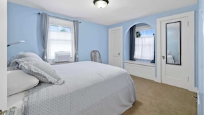 A bedroom with a bed, a bedside table, a window with curtains, a door, and a ceiling light. - Charming Apartment by Lakeside Park | Garden Views (Fort Wayne)