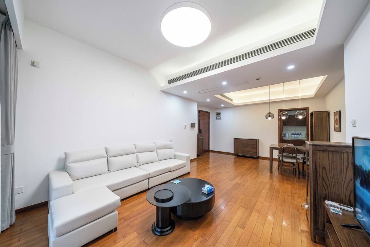 A modern living room with a white sectional sofa, a round coffee table, and a TV on a wooden stand.