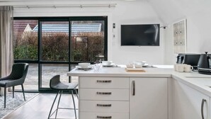 Eine moderne Küche mit einer großen Kochinsel, einem Essbereich mit Stühlen und Blick ins Freie durch große Fenster.